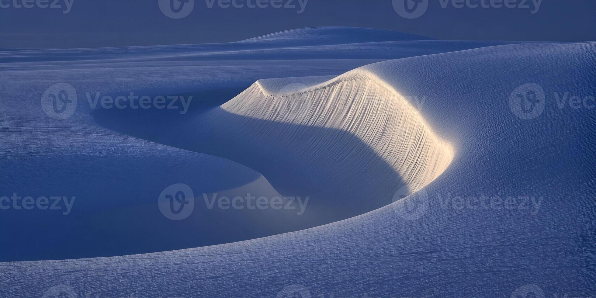 Sunlight illuminates the textured surface of a pristine blue snow dune creating abstract patterns photo