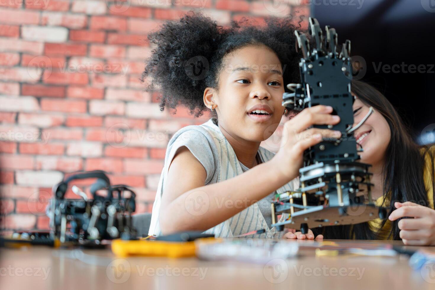 Young Girl Learning Robotics and Programming in a STEM Education Class, Students Examining a Robotic Arm Prototype, African American Child Engaged in Hands-on Tech Project with Teacher Guidance photo