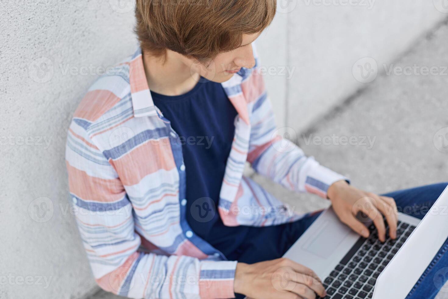 Cropped shot of stylish male student working at his course paper typing at laptop computer necessary information. Young boy using computer for surfing social networks using free internet conncetion photo