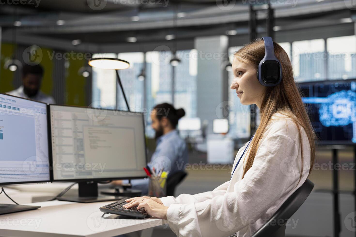 Young female programmer at work training machine learning models for anomaly detection automation. Tech startup employee wearing headphones, listening music and using artificial intelligence photo