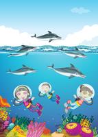 Delfines y niños nadando bajo el mar. vector