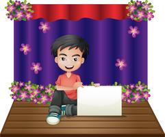 A smiling young boy sitting in the middle of the stage holding an empty signage vector