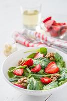 Salad with baby spinach, strawberry, nuts, oil, bread, plaid napkin
