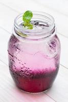 Jugo de uva roja refrigerado con refresco sobre tabla de madera blanca foto