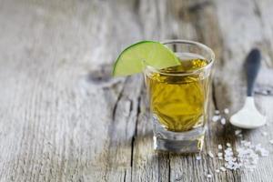 Tequila shot with lime and sea salt on rustic board