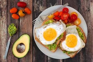 Healthy avocado, egg toasts with tomatoes on rustic wood background photo