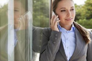 Businesswoman answering cell phone by glass door photo