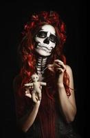 Young woman with calavera makeup (sugar skull) piercing voodoo doll photo