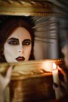 hermosa bruja sosteniendo una vela en la mano y mirando en el espejo foto