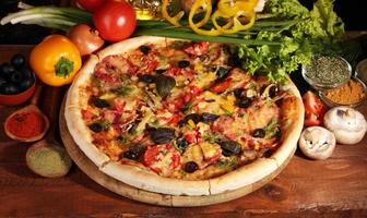 delicious pizza, vegetables and spices on wooden table photo