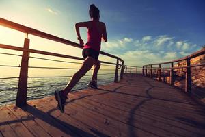 joven fitness mujer piernas corriendo en el paseo marítimo de madera junto al mar foto