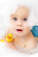 Foto del bebé en la bañera con pato de goma y espuma de baño en la cara