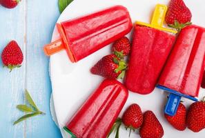 Bright strawberry popsicles with colorful sticks on the white pl photo