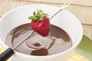 strawberry on fondue stick and melted chocolate bowl photo