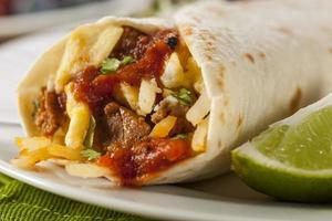Close-up of hearty chorizo breakfast burrito with lime