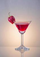 red cocktail garnished with strawberry in a martini glass