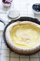Dutch baby pancake in skillet with powdered sugar and fruit photo