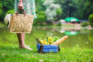 Picnic basket with fruits, bread and hat on straw bag photo