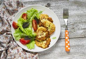 zucchini pancakes and fresh vegetable salad on white plate photo