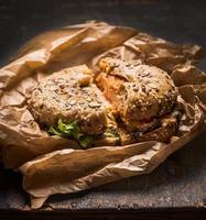 bun with chicken, cheese  lettuce  crumpled paper  rustic wooden background