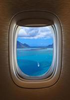 Airplane window with a view of a blue sea outside