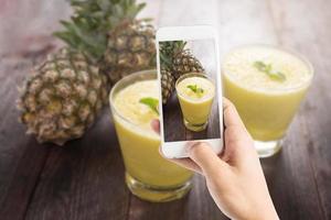 Taking photo of pineapple smoothie on wooden table
