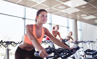 Group of happy women riding on exercise bikes in gym photo