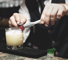 barman está decorando cóctel con cereza, imagen tonificada foto