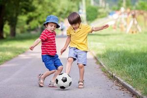 dos lindos niños pequeños, jugando al fútbol juntos, en verano