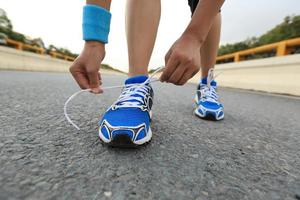 corredor de mujer joven atar cordones de los zapatos en la carretera de la ciudad foto
