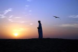 Silhouettes of an Arabian man and a bird at sunset photo