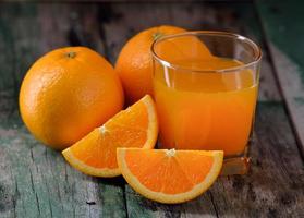 vaso de jugo de naranja y naranjas frescas en madera