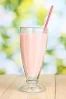 Pink milk shake on wooden table on bright background