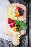 Berries, mint and melon on wooden cutting board