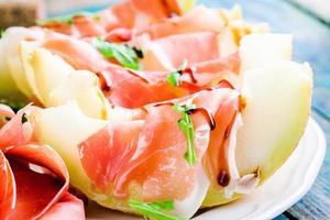 melon with slices of prosciutto, arugula and balsamic sauce closeup photo