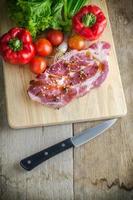 Raw pork on cutting board and vegetables knives.