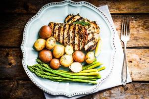 Grilled chicken with potatoes and asparagus on wooden background photo