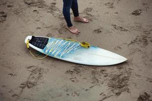 tabla de surf en la playa junto a las piernas de surfista. foto