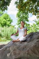 20 años chica rubia meditando debajo de un árbol en una roca foto