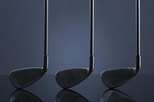 Golf clubs standing over reflective surface, isolated on dark background.