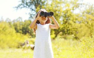 Little girl child looks in binoculars summer photo