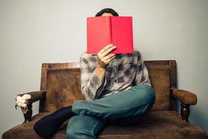 hombre escondiendo su rostro detrás del libro en el viejo sofá foto