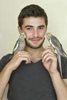 Young man holding two parrots on each hand