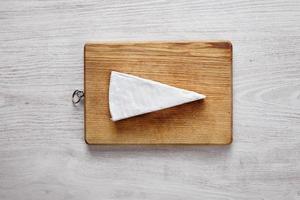 whole soft Brie isolated on choppping board white wooden table photo