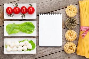 Tomatoes, mozzarella, pasta and green salad leaves with notepad photo