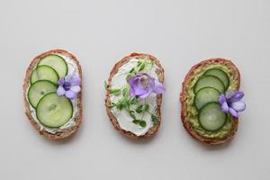 Green sourdough open face sandwiches with purple edible flowers