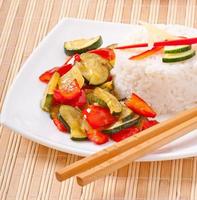 Plato de verduras arroz frito y palillos. foto