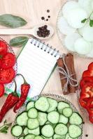 Fresh sliced vegetables with spices and a notebook for recipes.