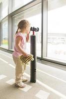 Little girl looking through binoculars in airport waiting room window