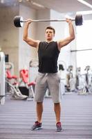 young man flexing muscles with barbell in gym photo